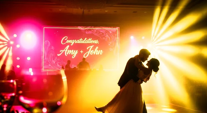 A couple dancing at a wedding ceremony, with a photowall of guest photos projected in the background